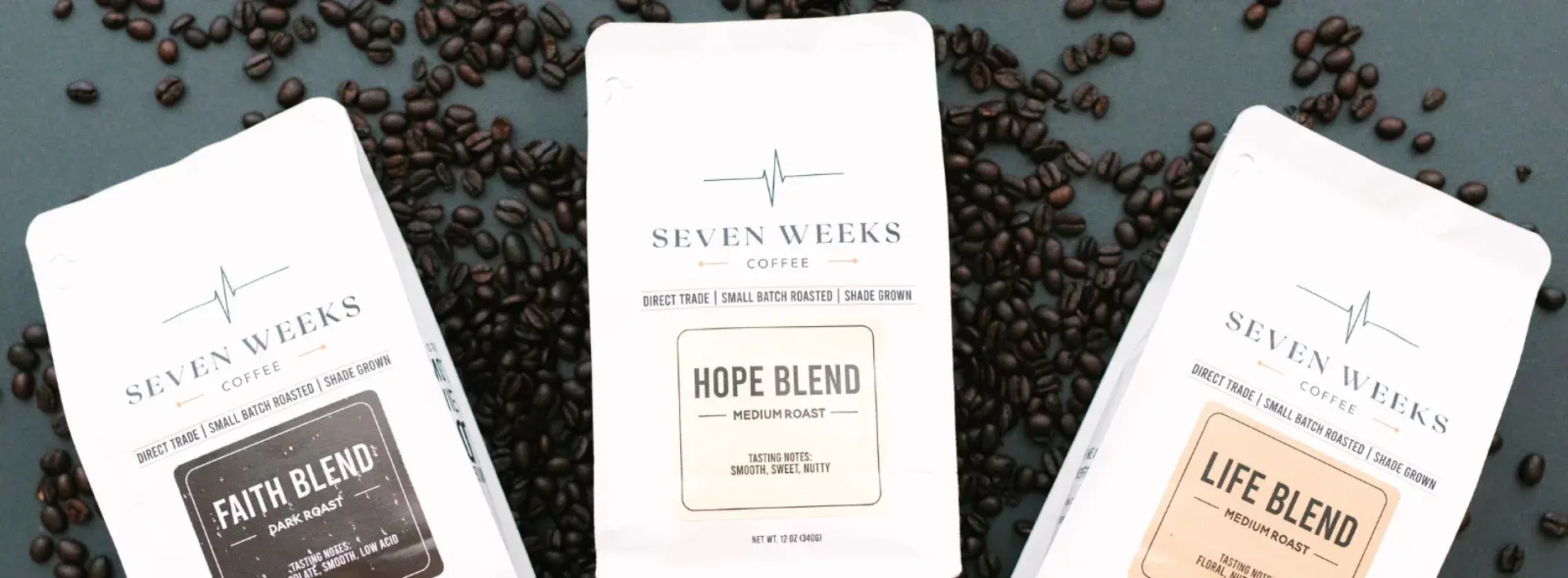 Seven Weeks Coffee Faith, Hope, and Life blend bags on a bed of coffee beans